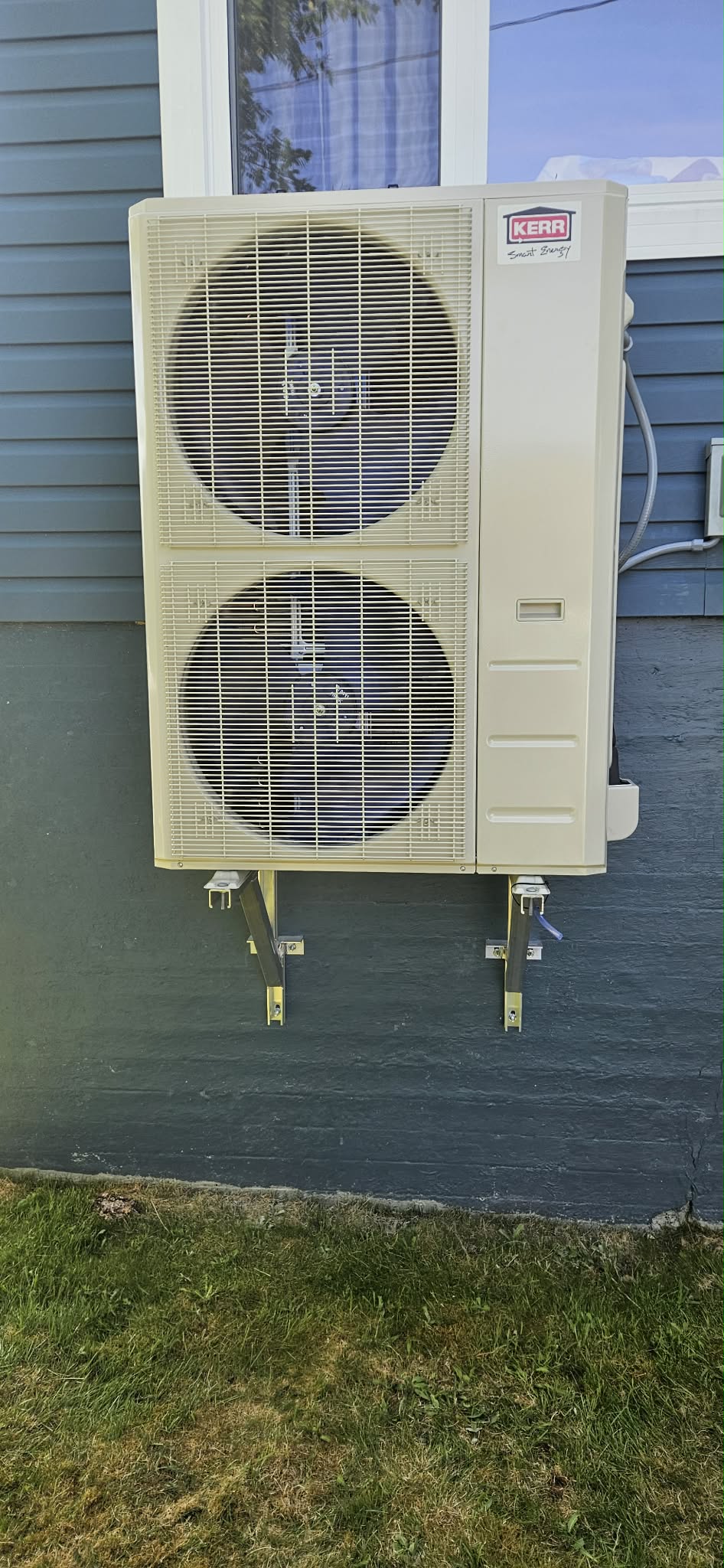 Kerr heat pump wall-bracket mounted on teal siding — summer install