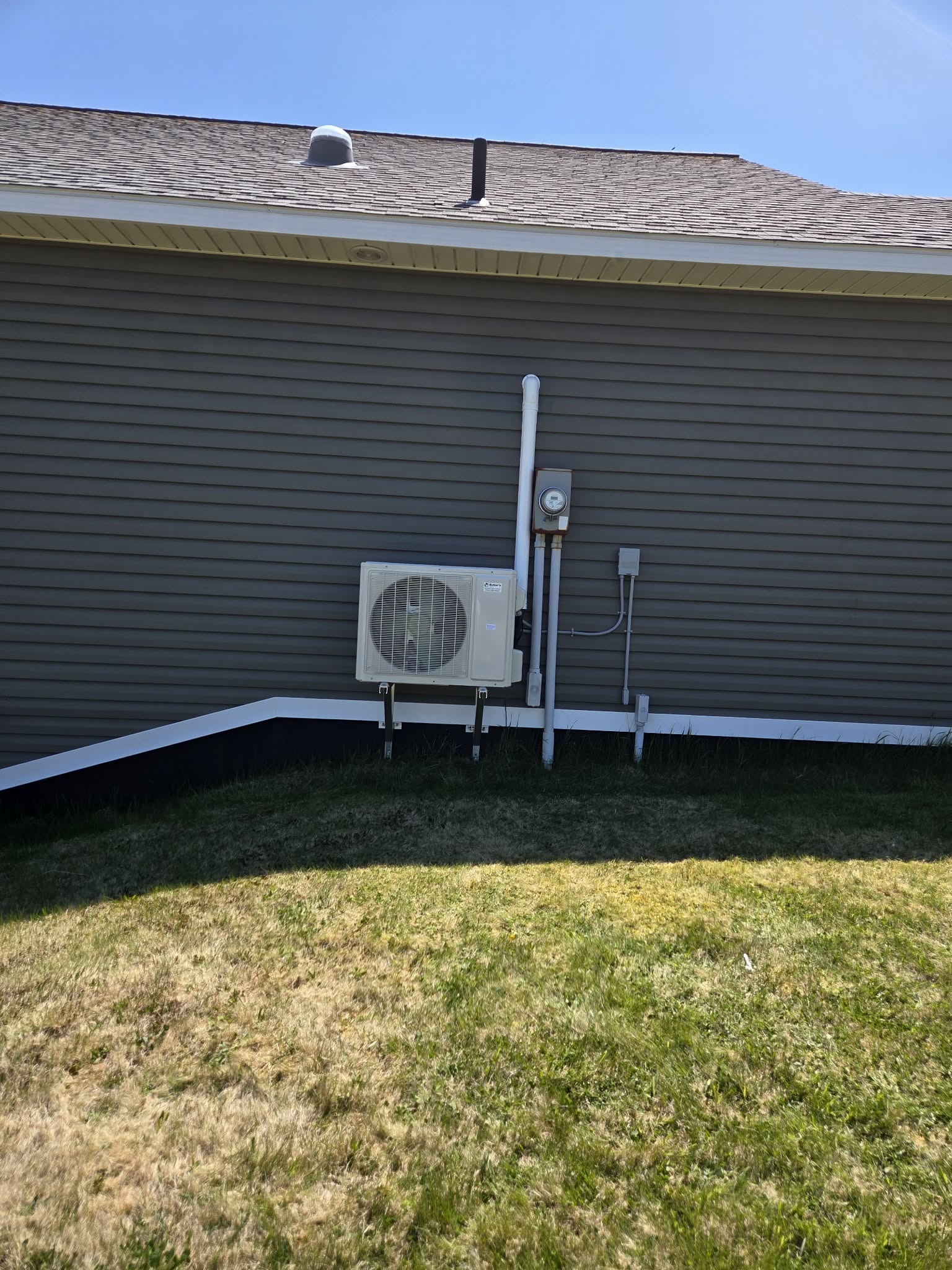 Mini split outdoor unit on grey siding — sunny day install
